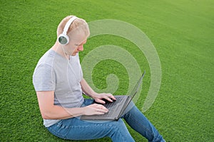 A young Caucasian man in a white T-shirt and headphones lies on an artificial lawn