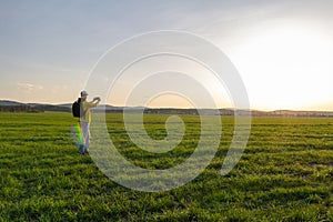 Young caucasian man in yellow jacket with backpack taking photo with mobile phone at sunset in czech spring landscape