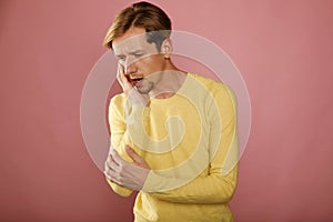 Young caucasian man in yellow sweater with toothache over pink background. Dentist healthcare concept