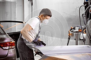 Young caucasian mechanic worker repairman sanding polishing car and preparing car for painting