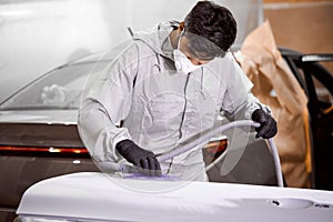 Young caucasian mechanic worker repairman sanding polishing car and preparing car for painting