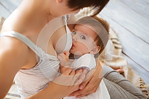 Young caucasian mom with infante in interior location. Mom nursing baby in a white bedroom. Nursery interior. Family at