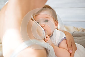 Young caucasian mom with infante in interior location. Mom nursing baby in a white bedroom. Nursery interior. Family at