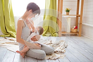 Young caucasian mom with infante in interior location. Mom nursing baby in a white bedroom. Nursery interior. Family at