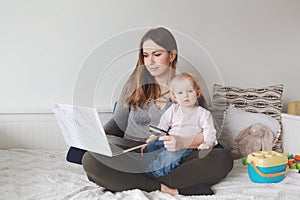Young Caucasian mother with baby shopping online from home. Stay at home single mom with kid toddler daughter buying ordering