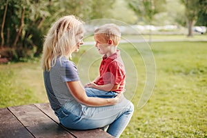 Young Caucasian mother and boy toddler son sitting together face to face. Family mom and child talking communicating outdoor on a photo