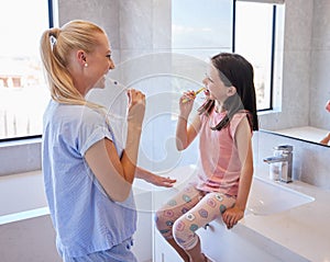 Young caucasian mother and her little daughter brushing their teeth with toothbrushes in the morning.Teaching your