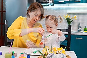 Young caucasian mother and her toddler daughter painting eggs. Concept of Easter celebration and traditions