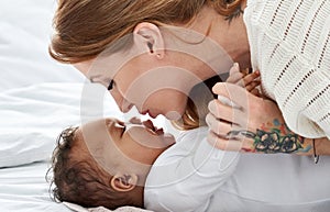Young caucasian mother kissing cute african american baby daughter lying in bed.