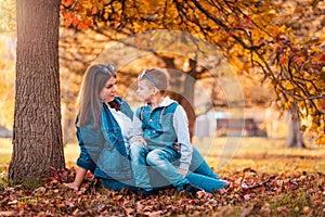 A young caucasian mother and son are sitting on golden leaves in an autumn park. The concept of a happy childhood and