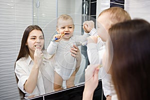 Young caucasian mother teaching baby boy how to brush teeth with toothbrush