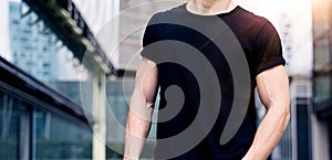 Young caucasian muscular man wearing black tshirt and jeans posing on the street of the modern city. Blurred background