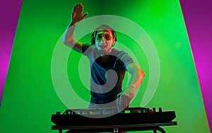 Young caucasian musician in headphones performing on bicolored green-purple background in neon light