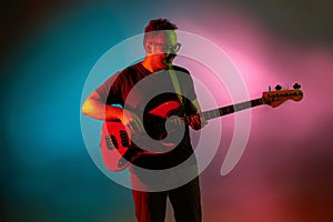 Young caucasian musician playing on gradient background in neon light. Concept of music, hobby, festival