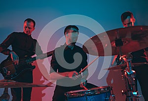 Young caucasian musicians, band performing in neon light on blue studio background