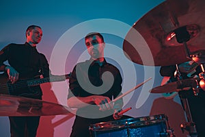 Young caucasian musicians, band performing in neon light on blue studio background
