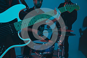 Young caucasian musicians, band performing in neon light on blue studio background, guitarist in front