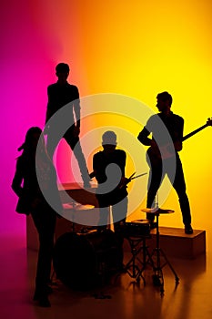 Young caucasian musicians, band performing in neon light on gradient studio background