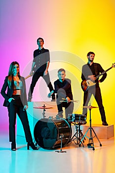 Young caucasian musicians, band performing in neon light on gradient studio background