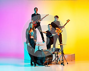 Young caucasian musicians, band performing in neon light on gradient studio background