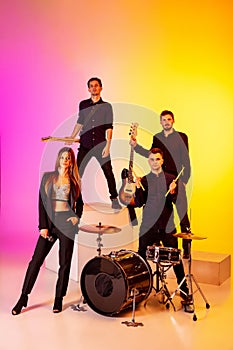 Young caucasian musicians, band performing in neon light on gradient studio background