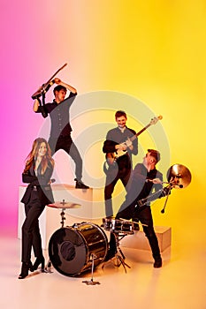 Young caucasian musicians, band performing in neon light on gradient studio background