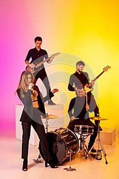 Young caucasian musicians, band performing in neon light on gradient studio background