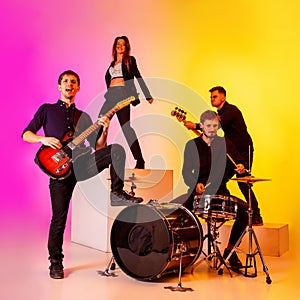 Young caucasian musicians, band performing in neon light on gradient studio background