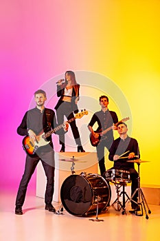 Young caucasian musicians, band performing in neon light on gradient studio background