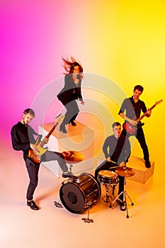 Young caucasian musicians, band performing in neon light on gradient studio background