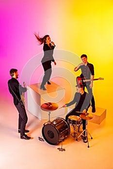 Young caucasian musicians, band performing in neon light on gradient studio background