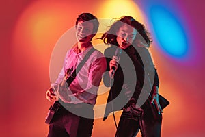 Young caucasian musicians, female singer and guitarist performing on gradient background in neon light. Concept of music