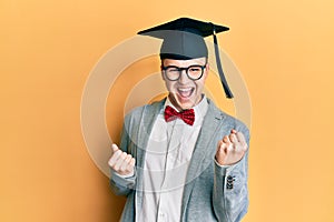 Young caucasian nerd man wearing glasses and graduation cap celebrating surprised and amazed for success with arms raised and eyes