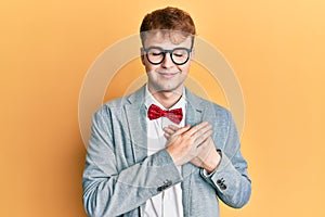 Young caucasian nerd man wearing glasses wearing hipster elegant look with bowtie smiling with hands on chest with closed eyes and