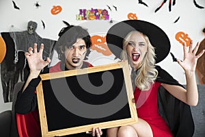 Young caucasian peoples in scary costumes or vampire clothes holding a blackboard, Halloween concept