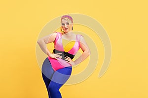 Young caucasian plus size female model`s training on yellow background