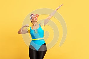 Young caucasian plus size female model`s training on yellow background