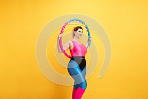 Young caucasian plus size female model`s training on yellow background