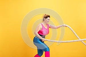 Young caucasian plus size female model`s training on yellow background