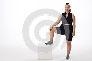 A young Caucasian plus-size model stands with one foot on white box, copy space