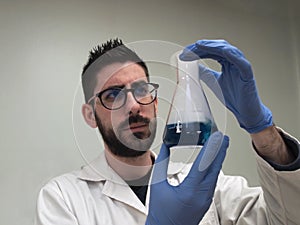 Young caucasian researcher is examining a flask with a blue liquid and dry ice inside