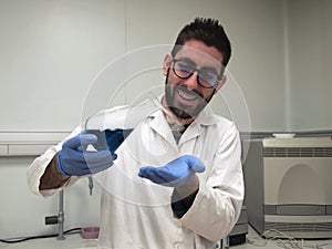 Young caucasian researcher is happily playing with a flask with a blue liquid and dry ice inside