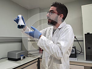 Young caucasian researcher is looking and talking at a flask with a blue liquid and dry ice inside