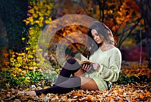 Young caucasian sensual woman reading a book in a romantic autumn scenery.Portrait of pretty young girl in autumnal forest