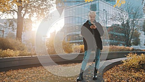 Young caucasian short haired blond woman using phone in the city park in front of office building in autumn