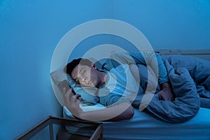 Young caucasian sleepless man bored in bed surfing on the Internet addicted to mobile phone