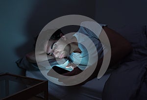 Young caucasian sleepless man bored in bed surfing on the Internet addicted to mobile phone