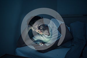 Young caucasian sleepless man bored in bed surfing on the Internet addicted to mobile phone