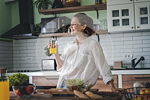 Young caucasian smiling woman drinking orange juice while standing in the kitchen at home