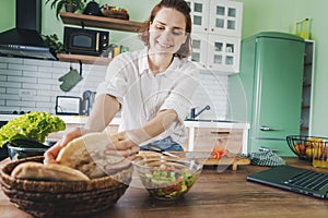 Young Caucasian smiling woman holding fresh bread in her hands while standing in the kitchen at home
